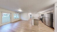 Located in Lynnwood, WA, this thoughtfully designed one-bedroom, one-bathroom residence offers a clean, modern aesthetic throughout its efficiently laid-out single floor. The open-concept living, dining, and kitchen area forms the heart of the home, anchored by warm light wood-tone flooring that flows throughout the main spaces. Large windows allow natural light to fill the living area, which also features a wall-mounted mini-split unit for year-round climate control.

The galley-style kitchen is equipped with stainless steel appliances — including a refrigerator, electric range, and over-the-range microwave — complemented by light wood cabinetry, neutral countertops, a double-basin sink, and track lighting overhead. A peninsula counter connects the kitchen to the dining and living space, making it ideal for everyday functionality.

The carpeted bedroom is generously sized, featuring two windows with views of the surrounding Lynnwood neighborhood, a ceiling fan with light, and access to two closets. The full bathroom includes a soaking tub and shower combo with a curved curtain rod, a vanity with storage, and light wood-tone flooring. A dedicated in-unit laundry room with side-by-side washer and dryer and built-in shelving adds everyday convenience. The unit also includes a private balcony and a hallway connecting all rooms seamlessly.