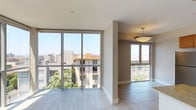Located on the fifth floor at 1907 Columbia in San Diego, this single-level residence offers a bright, open layout defined by dramatic floor-to-ceiling glass walls that frame sweeping panoramic views of the surrounding cityscape. Light pours in generously throughout the day, reflecting off the large-format tile flooring that runs throughout the main living areas, lending the space an airy, contemporary feel.

The open-concept living and dining area is spacious and versatile, anchored by the expansive window walls on two sides that create a wraparound visual connection to the San Diego skyline and neighboring neighborhoods. A door leads to a private outdoor balcony, extending the living space further.

The kitchen is well-appointed with warm honey-toned wood cabinetry, granite countertops, a center island with additional counter space and storage, and a full suite of stainless steel appliances including a gas range, microwave, refrigerator, and dishwasher. Recessed lighting highlights the clean, functional design.

The bathroom features a granite-topped vanity with an undermount sink, warm wood cabinetry, a wide mirror, and a separate glass-enclosed walk-in shower with tile surround. The light, neutral palette throughout the home creates a cohesive, calm ambiance that complements the vibrant urban setting just outside.