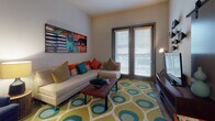 This single-floor residence offers a thoughtfully designed layout with distinct living spaces that balance modern style and everyday functionality. The kitchen is a standout area, featuring rich wood cabinetry, a deep navy tile backsplash, stainless steel appliances, and polished concrete floors that add an industrial edge. A peninsula with bar seating and a pendant light overhead creates an ideal spot for casual dining. The living room exudes energy and warmth, anchored by a bold geometric area rug in teal and green, a neutral sectional sofa adorned with vibrant accent pillows, and large glass doors that invite natural light and provide outdoor views. A striking piece of wall art adds a pop of color and personality to the space. The bedroom is a serene retreat with plush carpeting, large windows dressed in dark curtains, a ceiling fan, and warm ambient lighting. Thoughtful décor, including decorative mirrors and a rich wood dresser, complete the room's refined look. The full bathroom features a tiled tub-shower combo and a dark wood vanity, and flows directly into a generously sized walk-in closet outfitted with built-in shelving and hanging rods, offering excellent storage throughout.