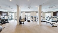 Located at 4021 Ridge Ave in Philadelphia's 19129 neighborhood, this fitness center offers a thoughtfully designed workout environment within a generously sized single-floor layout. The space features a neutral color palette of crisp whites and warm beige tones, complemented by a checkered low-pile carpet that adds subtle texture underfoot. Structural columns are integrated seamlessly into the floor plan, helping to define distinct workout zones without interrupting the open feel of the room.

Natural light pours in through large windows along the perimeter, offering views of the surrounding neighborhood and creating an airy, welcoming atmosphere. Recessed ceiling lighting and a ceiling fan ensure the space remains bright and comfortable during any workout. Full-length mirrors line one wall, visually expanding the room and allowing users to monitor their form.

The cardio section is well-stocked with treadmills, elliptical machines, upright and recumbent bikes, a StairMaster, and an AirRaid curved treadmill. A dedicated strength training area includes a cable machine, a rack of dumbbells, weight plates, and a flat bench, catering to a full range of training needs. The space is accessed through double glass doors and maintains a clean, modern aesthetic throughout.