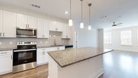 This well-designed single-story home in Port Wentworth, Georgia offers a clean, modern aesthetic throughout its two bedrooms and one bathroom. The open-concept kitchen is a standout feature, showcasing white shaker cabinetry, granite countertops, a subway tile backsplash, stainless steel appliances, and a large center island with pendant lighting — ideal for both cooking and entertaining. Wood-look flooring flows through the kitchen and into the spacious living room, which is bathed in natural light from a trio of windows and accented by a ceiling fan overhead.

The two bedrooms are carpeted for comfort, with the generously sized primary bedroom offering ample space and a walk-in closet complete with built-in wire shelving. The second bedroom features a large window with outdoor views, filling the room with natural light. The bathroom is finished with matching granite countertops, a dark wood vanity, wood-look flooring, and a glass-enclosed walk-in shower. A hallway connects the living areas to the bedrooms, contributing to the home's efficient and practical layout. The overall ambiance is bright, clean, and move-in ready, reflecting a contemporary design sensibility throughout.