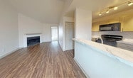 This single-story, one-bedroom, one-bathroom unit at 1540 Chenault offers a well-designed layout with a clean, modern aesthetic. The living area immediately draws attention with its dramatic vaulted ceilings, which lend an open, airy feel to the space. A corner fireplace with a white mantel serves as a focal point, complementing the rich, wood-style plank flooring that extends throughout the main living areas.

The kitchen is positioned adjacent to the living space and is separated by a breakfast bar featuring marble-look countertops. The kitchen includes white cabinetry with sleek hardware, a matching marble-look backsplash in a herringbone pattern, and black appliances including a range and over-the-range microwave. Track lighting illuminates the workspace effectively.

The entry area provides a welcoming transition into the unit, with recessed lighting and a windowed door that allows natural light to filter in. The bedroom is carpeted and generously proportioned, offering a quiet retreat from the main living area.

The bathroom features an extended marble-look vanity countertop with ample surface space, a large mirror, and a separate enclosed wet area with a tub/shower combination. Wood-style flooring continues into the bathroom, maintaining a cohesive look throughout the unit.