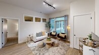 This contemporary apartment offers 1050 square feet of thoughtfully designed living space. The open-concept layout seamlessly integrates the kitchen, living, and dining areas, creating a spacious and inviting atmosphere. The kitchen is a highlight, featuring crisp white cabinetry, stainless steel appliances, and a practical L-shaped design with ample counter space.

The living room is bathed in natural light from large windows, offering views of the surrounding area. It's furnished with modern pieces, including a plush area rug, stylish seating, and a sleek entertainment unit. The primary bedroom, measuring 230 square feet, provides a tranquil retreat with neutral tones and minimalist decor. The second bedroom is equally well-appointed, featuring clean lines and a calming color palette.

Both bathrooms showcase modern fixtures, with one featuring a glass-enclosed shower and wooden vanity. Throughout the apartment, wood-look flooring adds warmth and continuity. The overall design aesthetic is clean and uncluttered, with a focus on functionality and comfort. Subtle decorative elements and indoor plants add personality to the space, creating a welcoming home environment.