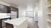 The Savoye 2 Plan A1C is a thoughtfully designed 680-square-foot, one-bedroom, one-bathroom apartment spread across a single floor. The open-concept kitchen and living area serves as the heart of the unit, featuring rich dark espresso cabinetry that extends to the ceiling, crisp white quartz countertops, a subway tile backsplash, and a full suite of stainless steel appliances including a refrigerator, range, microwave, and dishwasher. A central kitchen island provides additional prep space and casual seating. Wood-style plank flooring runs consistently throughout the entire unit, lending a warm, cohesive aesthetic. The living area is bright and open, equipped with a ceiling fan and ample wall space for flexible furniture arrangements. The 150-square-foot primary bedroom offers natural light through multiple windows with blinds, a ceiling fan, and dedicated closet space. The bathroom continues the unit's modern design language with a dark vanity, white countertop, a large mirror, and wood-style flooring. A dedicated closet adds practical storage. Crisp white walls and clean architectural lines throughout create a contemporary, move-in-ready atmosphere ideal for comfortable everyday living.