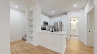 This thoughtfully designed 1-bedroom, 1-bathroom residence offers a clean, modern aesthetic throughout, anchored by light-toned hardwood flooring and crisp white walls that create a bright, airy ambiance. The open-concept kitchen and living area form the heart of the home, with the kitchen showcasing white shaker cabinetry accented by matte black hardware, a herringbone tile backsplash, stainless steel appliances including a refrigerator, range, and microwave, and a white quartz peninsula with an undermount sink and black faucet. A set of built-in open shelves adds both style and function near the kitchen. The spacious living room flows seamlessly from the kitchen and is bathed in natural light through a set of French doors that open to the outdoors. The bedroom is a comfortable retreat, featuring a ceiling fan, a window with garden views, and access to a dedicated walk-in closet with wire shelving for ample storage. The full bathroom is elegantly finished with large-format tile flooring, a dual-sink white vanity with black-framed mirrors, and a glass-enclosed soaking tub and shower combination. Recessed lighting throughout completes the polished, move-in-ready feel of this well-proportioned residence.