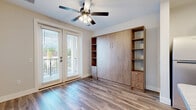 Located at 484 Lazelle Rd in Columbus, OH, this efficiently designed studio unit makes excellent use of its single-floor layout. The combined kitchen and living area serves as the heart of the space, featuring warm wood-look luxury vinyl plank flooring that runs throughout. The kitchen is outfitted with stainless steel appliances, including a range, over-the-range microwave, and refrigerator, complemented by white shaker-style cabinetry, a subway tile backsplash, and a marble-look countertop peninsula with a built-in sink — ideal for both meal prep and casual dining. Pendant lighting above the peninsula adds a modern touch. A built-in murphy bed unit with open wood shelving and integrated drawers provides smart, space-saving sleeping and storage solutions. French doors flood the living area with natural light and open to a private balcony with outdoor views, while a ceiling fan ensures year-round comfort. The bathroom features a white vanity with ample cabinet storage, a large mirror, and a dedicated walk-in shower. A utility area accommodates an in-unit washer and dryer, adding everyday convenience. A closet and entrance area complete this thoughtfully arranged, move-in ready studio.