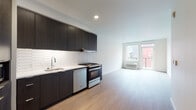Located at 1725 SW Salmon St in Portland, Oregon's Goose Hollow neighborhood, this contemporary single-floor unit offers a thoughtfully designed open layout with clean lines and modern finishes throughout. Light wood-tone flooring runs continuously across the space, contributing to a cohesive and airy feel.

The kitchen is a standout feature, outfitted with rich dark wood cabinetry that extends to the ceiling for ample storage, stainless steel appliances including a gas range and dishwasher, a white quartz countertop, and a striking elongated hexagonal tile backsplash that adds a modern geometric detail. A built-in microwave and refrigerator complete the well-equipped space.

The open living area benefits from large windows and direct access to a private balcony, allowing natural light to fill the room and providing views of the surrounding urban streetscape. A wall-mounted HVAC unit ensures year-round comfort.

The bathroom features a dark wood vanity with a white countertop, an undermount sink, and a large mirror with overhead lighting — maintaining the same refined, contemporary aesthetic found throughout the unit.

A dedicated hallway leads to a discreet in-unit laundry closet housing a full-size stacked washer and dryer, adding a high level of everyday convenience. The overall design is clean, modern, and functional, making this an efficient and well-appointed urban residence.