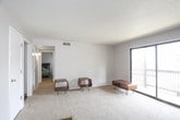 This single-floor unit offers a practical and functional layout spread across several well-defined rooms. The living area is generously sized, featuring neutral-toned carpet flooring, light gray walls, and a textured ceiling. A large sliding glass door fitted with vertical blinds floods the space with natural light and provides direct access to an outdoor area, creating an open and airy atmosphere.

The kitchen is efficiently designed with dark espresso-toned cabinetry spanning both upper and lower sections, offering ample storage. It includes a full-size refrigerator, a white electric range with an overhead microwave, a double-basin sink, and laminate countertops. Rich wood-look flooring anchors the kitchen, providing a clean contrast to the darker cabinetry.

The unit features multiple bedrooms, each finished with wall-to-wall carpet and neutral gray walls under textured ceilings. One bedroom includes a set of large dark-paneled sliding closet doors that add a bold design element, while other bedrooms feature windows dressed with blinds that bring in natural light. The floor plan, as visible in the dollhouse view, reveals a compact and efficiently organized layout with clear separation between living, sleeping, and kitchen spaces, and multiple interior doors providing privacy throughout.