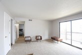 This single-floor unit offers a practical and functional layout spread across several well-defined rooms. The living area is generously sized, featuring neutral-toned carpet flooring, light gray walls, and a textured ceiling. A large sliding glass door fitted with vertical blinds floods the space with natural light and provides direct access to an outdoor area, creating an open and airy atmosphere.

The kitchen is efficiently designed with dark espresso-toned cabinetry spanning both upper and lower sections, offering ample storage. It includes a full-size refrigerator, a white electric range with an overhead microwave, a double-basin sink, and laminate countertops. Rich wood-look flooring anchors the kitchen, providing a clean contrast to the darker cabinetry.

The unit features multiple bedrooms, each finished with wall-to-wall carpet and neutral gray walls under textured ceilings. One bedroom includes a set of large dark-paneled sliding closet doors that add a bold design element, while other bedrooms feature windows dressed with blinds that bring in natural light. The floor plan, as visible in the dollhouse view, reveals a compact and efficiently organized layout with clear separation between living, sleeping, and kitchen spaces, and multiple interior doors providing privacy throughout.
