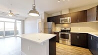 Located at 1051–1055 S Broadway in Denver, CO, this single-floor residential unit offers a thoughtfully designed layout with modern finishes throughout. The kitchen is a standout feature, showcasing dark espresso cabinetry that extends to the ceiling, a crisp white tile backsplash, light quartz countertops, and a full suite of stainless steel appliances including a refrigerator, range, microwave, and dishwasher. A peninsula with a white countertop provides additional prep space and casual seating, while a pendant light adds an industrial-chic touch overhead. Wood-look flooring runs throughout the kitchen and main living areas, lending warmth and continuity to the space. The open living area is bright and airy, benefiting from natural light streaming through a sliding glass door that leads to a private balcony. Two well-proportioned bedrooms feature plush carpeting, ceiling fans, and broad windows that frame outdoor views. Both bathrooms are finished with wood-look flooring and include soaking tubs with tiled surrounds. The unit's neutral color palette and clean architectural lines create a cohesive, contemporary atmosphere that is both functional and inviting.