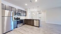 This single-floor unit offers a thoughtfully designed layout with modern finishes throughout. The kitchen serves as a central highlight, featuring dark espresso cabinetry, granite countertops, a classic white subway tile backsplash, and a full suite of stainless steel appliances including a refrigerator, electric range, over-the-range microwave, and dishwasher. A peninsula with pendant lighting above provides additional prep space and flows naturally into the open living area, which is finished with light wood-style flooring and a ceiling fan, with sliding door access to a private balcony overlooking a green outdoor view. The bedroom spaces are carpeted for comfort and include a ceiling fan, while a generous walk-in closet with built-in shelving and hanging rods provides ample storage. The bathrooms are finished with wood-look tile flooring, granite-topped vanities with shaker-style cabinetry, large mirrors, and tiled tub-shower combinations. Clean white walls and recessed lighting throughout contribute to a bright, contemporary ambiance that feels open and move-in ready.