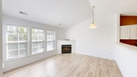 Located at 2260 Golden Garden Circle in Chester, VA, this two-story home offers a well-designed layout across two levels. The main living area is bright and airy, showcasing light hardwood-style flooring, vaulted ceilings, and an abundance of natural light streaming through multiple windows. A corner fireplace serves as a focal point in the living room, complemented by a pendant light fixture that adds a touch of warmth. The open-concept kitchen overlooks the living space through a pass-through counter, featuring white cabinetry, stainless steel appliances including a refrigerator, electric range, and over-the-range microwave, and tile flooring. Carpeted stairs with a warm wood handrail lead to the upper level, where both bedrooms are located. The spacious primary bedroom includes a sliding glass door opening to an outdoor deck, an additional window for natural light, and a closet. The second bedroom is carpeted with a double-door closet. Both bathrooms are finished with tile flooring, white vanities, and tub-shower combinations. The home's clean, neutral palette throughout creates a move-in ready environment that is both functional and inviting.