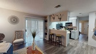 This thoughtfully designed 1-bedroom, 1-bathroom residence offers an efficient and functional single-floor layout that maximizes every square foot of living space. Hardwood-style flooring flows consistently throughout, tying the living, dining, and kitchen areas together seamlessly.

The living room serves as a welcoming focal point, featuring a textured ceiling, neutral gray walls, and a front entry door. A large sliding glass door floods the space with natural light and provides direct access to the exterior.

The kitchen is a functional galley-style layout with gray cabinetry, light countertops, a mosaic tile backsplash, and black appliances including a refrigerator and electric range. A peninsula with bar-top seating extends into the living area, creating an open, connected feel ideal for everyday dining or casual entertaining. A dedicated dining nook with distinctive wall décor completes the common living areas.

The bedroom is a comfortable retreat with a ceiling fan, a window with blinds for natural light control, and a closet. The bathroom features a full soaking tub and shower combination with clean white surroundings and wood-style flooring.

Overall, the unit presents a cohesive, modern aesthetic with practical finishes throughout.