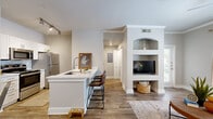 This thoughtfully designed one-bedroom, one-bathroom residence offers an efficient and cohesive layout across a single floor. The open-concept living, dining, and kitchen area serves as the heart of the home, featuring warm wood-look flooring that flows throughout. The kitchen is equipped with stainless steel appliances — including a refrigerator, range, microwave, and dishwasher — alongside white cabinetry and light countertops. A peninsula with bar seating connects the kitchen to the living area, creating a functional and social space. The living room showcases a standout built-in shelving unit with an arched upper niche and a dedicated media alcove, adding architectural character. Natural light enters through windows and a glass-panel front door. A separate dining area features wainscoting and crown molding, lending a refined touch. The bedroom is a comfortable retreat with a window, hardwood-style flooring, and direct access to both the bathroom and a walk-in closet fitted with wire shelving. The bathroom includes a full soaking tub and shower combination with floor-to-ceiling tile surround. Two hallways connect the spaces efficiently, completing this compact yet well-appointed home.