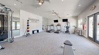 The Fairpointe at Gulf Breeze Fitness Center is a thoughtfully designed, single-floor community gym that offers a comprehensive workout environment. The space is finished with light gray carpet tiles and crisp white walls, including a distinctive shiplap accent wall prominently displaying "The Fairpointe at Gulf Breeze" branding, lending the room a clean, modern aesthetic.

The cardio section features multiple treadmills and an elliptical trainer, each positioned in front of wall-mounted flat-screen televisions for an engaging workout experience. A stationary spin bike rounds out the cardio offerings. For strength training, the fitness center includes a multi-functional cable and rack system, a dedicated dumbbell rack with a full set of free weights, a medicine ball tower with assorted weighted balls, and a weight bench. Large mirrors along the walls enhance the sense of space and support proper form during exercise.

Natural light filters in through several windows, while recessed ceiling lights and dual ceiling fans with built-in lighting ensure the room remains bright and well-ventilated. A set of double glass doors provides a welcoming entrance with views to the exterior. The overall ambiance is clean, functional, and inviting, making it a well-rounded amenity for residents seeking a convenient and fully equipped place to exercise.