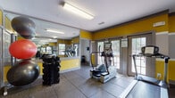 Located at 3920 Club Dr in Duluth, Georgia, this fitness center is a well-equipped, single-floor facility designed to support a well-rounded workout routine. The space immediately stands out with its bold color scheme — vibrant yellow accent walls paired with gray trim create an energetic and motivating atmosphere throughout.

The gym is outfitted with a solid selection of cardio equipment, including multiple treadmills and an elliptical trainer, as well as a stationary recumbent bike and a weight bench for strength training. A rack of dumbbells and a collection of stability and medicine balls round out the available equipment, offering users versatility in their workouts.

Durable rubber flooring covers the entire space, providing both safety and comfort underfoot. Large floor-to-ceiling mirrors line one wall, visually expanding the room and allowing users to monitor their form during exercise. The mirrors also enhance the sense of openness in the space.

Natural light filters in through multiple windows and glass-paneled doors that open to the outdoors, creating a bright and inviting environment. Overhead fluorescent lighting ensures the space remains well-lit at all hours. The layout is practical and efficiently organized, with clear circulation paths between equipment. Overall, this fitness center offers a functional and energizing environment for residents seeking convenient on-site exercise facilities.