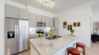 This well-appointed two-bedroom, three-bathroom residence features a clean, modern design throughout its single-floor layout. Light wood-tone flooring and crisp white walls run throughout, creating a bright and cohesive aesthetic. The open-concept kitchen is a standout feature, equipped with stainless steel appliances, gray shaker-style cabinetry, a white subway tile backsplash, and a granite-topped island with bar seating — ideal for both cooking and casual dining. Track lighting overhead enhances the workspace. Adjacent to the kitchen, the dining area benefits from large windows that welcome ample natural light, while the living room offers generous wall space and additional windows with outdoor views. A well-lit hallway connects the living areas to the private quarters, where both bedrooms feature large windows, high ceilings, and comfortable proportions. The primary bedroom is accompanied by a spacious walk-in closet with built-in shelving and hanging rods. The three bathrooms include neutral tile work and a soaking tub, providing a clean, functional finish. Two dedicated closets offer additional storage throughout the unit. The overall ambiance is modern and airy, with consistent finishes that lend a polished, move-in-ready feel.