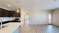 This single-floor residence offers a thoughtfully designed layout comprising two bedrooms, three bathrooms, a kitchen, a hallway, and a dedicated closet. The open-concept living and kitchen area forms the heart of the home, featuring light-toned hardwood-style flooring that extends throughout the main living spaces. The kitchen is equipped with dark espresso cabinetry reaching toward the ceiling, providing ample storage, complemented by white countertops, stainless steel appliances including a range, microwave, and refrigerator, and a peninsula with an integrated sink ideal for casual dining or meal preparation. A pendant light fixture adds a focused accent above the workspace.

The living area is bright and open, with natural light entering through multiple windows offering views of the surrounding exterior. Both bedrooms are carpeted and well-sized, with the primary bedroom featuring a spacious walk-in closet outfitted with wire shelving and hanging rods. The second bedroom includes a sliding-door closet with built-in shelving. One bathroom conveniently integrates in-unit washer and dryer connections alongside a vanity with dark cabinetry and white countertop. Additional bathrooms include a glass-enclosed shower with chrome grab bars, reinforcing accessibility throughout the residence.