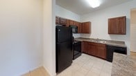 This single-floor unit at 520 Nathans Way in Grand Haven, Michigan, offers a straightforward and functional layout designed for comfortable everyday living. The open-concept living and kitchen area forms the heart of the space, where light-toned carpet in the living room transitions seamlessly to tile flooring in the kitchen. A half-wall peninsula divides the two areas, providing both visual separation and additional counter space.

The kitchen is well-equipped with rich, dark wood cabinetry offering ample storage, granite-style countertops, a double stainless steel sink, and black appliances including a refrigerator, range, microwave, and dishwasher. Tile flooring runs throughout the kitchen, adding durability to the space.

The carpeted bedroom is generously sized, featuring a large window dressed with vertical blinds that allows natural light to filter in. The neutral wall tones and panel-style door contribute to a clean, understated aesthetic throughout.

The bathroom includes a vanity with dark wood cabinetry, a granite-style countertop, an integrated sink, a large mirror, and a tub-shower combination. Light tile flooring ties the bathroom together with the rest of the unit's practical design.
