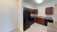 This single-floor unit at 520 Nathans Way in Grand Haven, Michigan, offers a straightforward and functional layout designed for comfortable everyday living. The open-concept living and kitchen area forms the heart of the space, where light-toned carpet in the living room transitions seamlessly to tile flooring in the kitchen. A half-wall peninsula divides the two areas, providing both visual separation and additional counter space.

The kitchen is well-equipped with rich, dark wood cabinetry offering ample storage, granite-style countertops, a double stainless steel sink, and black appliances including a refrigerator, range, microwave, and dishwasher. Tile flooring runs throughout the kitchen, adding durability to the space.

The carpeted bedroom is generously sized, featuring a large window dressed with vertical blinds that allows natural light to filter in. The neutral wall tones and panel-style door contribute to a clean, understated aesthetic throughout.

The bathroom includes a vanity with dark wood cabinetry, a granite-style countertop, an integrated sink, a large mirror, and a tub-shower combination. Light tile flooring ties the bathroom together with the rest of the unit's practical design.