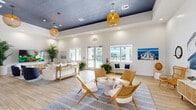 Located at 3640 Blue Fin Way in Fort Myers, Florida, this single-story community clubhouse delivers a cohesive coastal aesthetic across its generously sized floor plan. Light wood-style flooring flows throughout, unifying the multiple living and lounge areas that make up the heart of the space.

The welcoming entry features double glass doors that open to outdoor views, with large windows that frame the community pool and allow natural light to pour in. A bold blue-and-white tropical palm leaf wallcovering makes an immediate design statement, setting the tone for the nautical theme carried throughout.

The main gathering area is anchored by a white shiplap accent wall adorned with marine-inspired artwork, porthole mirrors, and a large boat mural. Woven rattan seating, woven pendant lighting, and a navy-accented color palette reinforce the seaside ambiance. Elevated ceilings with a painted navy tray detail add architectural interest overhead.

A dedicated wet bar area features a white countertop with bar-height seating, a mini refrigerator, and compass and fish-themed wall décor. A separate media lounge offers a large-screen TV, a light wood media console, and comfortable seating surrounded by lush indoor palms. The hallway connects all zones efficiently, ensuring smooth circulation throughout the clubhouse.