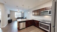 Located at 801 W 4th Ave in Stillwater, Oklahoma, this 2-bedroom, 2-bathroom unit offers a well-organized single-floor layout designed for comfortable everyday living. The open kitchen and living area serves as the heart of the unit, where the kitchen stands out with rich dark-stained cabinetry, granite countertops, stainless steel appliances including a refrigerator, gas range, and microwave, and a peninsula with bar seating illuminated by a pendant light. Wood-style flooring runs through the main living areas, complementing the neutral wall tones throughout. The living room provides a bright, open feel with a ceiling fan, natural light from a large window, and wall-mounted TV setup. Both bedrooms feature plush carpeting, ceiling fans, and windows that bring in natural light. The primary bedroom offers a notably spacious footprint with ample room for furnishings. The two bathrooms are finished with wood-look flooring, dark vanity cabinetry, and white countertops; one includes a full tub/shower combination. A dedicated in-unit laundry space houses a full-size front-loading washer and dryer set with overhead shelving, adding a practical and convenient amenity to this thoughtfully designed residence.