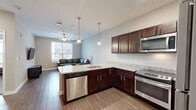Located at 801 W 4th Ave in Stillwater, Oklahoma, this 2-bedroom, 2-bathroom unit offers a well-organized single-floor layout designed for comfortable everyday living. The open kitchen and living area serves as the heart of the unit, where the kitchen stands out with rich dark-stained cabinetry, granite countertops, stainless steel appliances including a refrigerator, gas range, and microwave, and a peninsula with bar seating illuminated by a pendant light. Wood-style flooring runs through the main living areas, complementing the neutral wall tones throughout. The living room provides a bright, open feel with a ceiling fan, natural light from a large window, and wall-mounted TV setup. Both bedrooms feature plush carpeting, ceiling fans, and windows that bring in natural light. The primary bedroom offers a notably spacious footprint with ample room for furnishings. The two bathrooms are finished with wood-look flooring, dark vanity cabinetry, and white countertops; one includes a full tub/shower combination. A dedicated in-unit laundry space houses a full-size front-loading washer and dryer set with overhead shelving, adding a practical and convenient amenity to this thoughtfully designed residence.