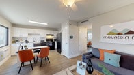This single-floor unit at Mountain Run offers a practical and thoughtfully designed layout across an open, connected living space. The living room serves as the central hub, featuring wood-look laminate flooring, a ceiling fan, and a glass-panel exterior door that invites natural light from outside. The space comfortably accommodates seating arrangements and flows directly into the dining and kitchen areas.

The kitchen is outfitted with white shaker-style cabinetry, light quartz countertops, and a classic white subway tile backsplash. Black appliances — including an electric range with overhead ventilation, refrigerator, dishwasher, and microwave — provide a striking contrast to the clean, bright cabinetry. A frosted-glass door from the kitchen leads to an in-unit laundry area, adding everyday convenience.

The bedrooms are cozy and well-lit, each featuring wood-look flooring, neutral-toned walls, and windows fitted with blinds that allow adjustable natural light. The rooms provide ample space for sleeping and study areas. A smart home panel is visible near the main entry, and HVAC vents throughout ensure year-round comfort. The overall ambiance is modern, clean, and functional.