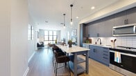 Located at 2141 Waterside Drive in Nashville, TN, this contemporary 2-bedroom, 2-bathroom residence offers a thoughtfully designed open-concept floor plan filled with natural light and upscale finishes throughout. The kitchen is a standout centerpiece, featuring slate-blue cabinetry, white subway tile backsplash, stainless steel appliances, and a large quartz-topped island with seating for multiple guests, illuminated by striking glass pendant lights. The kitchen flows seamlessly into the living area, where floor-to-ceiling windows frame sweeping views of the Nashville skyline and surrounding greenery, creating a bright and airy atmosphere. Light wood-style flooring runs throughout the main living areas, adding warmth and continuity. Both bedrooms are generously proportioned, each benefiting from large windows with scenic outdoor views. The primary bedroom offers direct balcony access, plush carpeting, and a spacious walk-in closet with built-in shelving. The two bathrooms mirror the home's refined aesthetic, featuring blue-gray vanities with quartz countertops, black hardware accents, and tiled tub-shower combinations. Two dedicated closets provide ample storage throughout the residence, completing this well-appointed Nashville home.