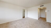 This single-story unit at 511 E Sahara Avenue in Las Vegas offers a practical and well-organized layout across three bedrooms and one bathroom. The floor plan, visible in the 3D model, illustrates a logical flow from the living area through a connecting hallway to the bedrooms, with the kitchen positioned centrally.

The living room is bright and welcoming, featuring plush wall-to-wall carpeting, a large window with vertical blinds that invites natural light and outdoor views of surrounding greenery, and a front entry door. The neutral white walls and textured ceiling contribute to a clean, open atmosphere.

The primary bedroom is notably spacious, fitted with carpet, a ceiling fan with integrated lighting, a window with vertical blinds, and a wide wall-spanning closet with louvered bifold doors providing generous storage. The additional bedrooms are similarly carpeted and include ceiling fans, windows for natural light, and individual closets—one featuring a walk-in configuration.

The shared bathroom is finished with tile flooring, a white vanity with sink, and a tiled shower-tub combination with a curved curtain rod and a small window for ventilation. Throughout the unit, the consistent use of neutral tones, carpet, and functional fixtures creates a cohesive and practical living environment.