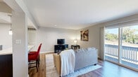 This single-floor residence offers a functional and well-designed layout across a comfortable footprint. The open-concept living room features warm hardwood-style flooring, neutral gray walls, recessed lighting, and a sliding glass door that floods the space with natural light while providing direct access to a private balcony with outdoor views. The combined kitchen and dining area is a standout feature, showcasing dark espresso cabinetry, light granite countertops, a tile backsplash, black appliances including a range, built-in microwave, and dishwasher, as well as a skylight that brightens the workspace. The spacious bedroom is finished with plush carpeting and offers ample room for a full furniture arrangement, complemented by two closets for generous storage. The bathroom features dark wood cabinetry with a single vanity, a large mirror, tile flooring, and a shower-tub combination. A dedicated utility room houses a stacked washer and dryer, adding everyday convenience. A hallway connects the rooms with an efficient flow, completing this practical and comfortable single-level home.