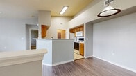 This two-floor residence offers a thoughtfully designed layout with a blend of functional spaces and practical finishes throughout. The heart of the home is an open-concept kitchen and living area, where soaring vaulted ceilings create an airy, expansive feel. The kitchen features warm honey-toned wood cabinetry, light tile flooring, a full suite of white appliances including a refrigerator, electric range, and built-in microwave, and a peninsula with a sink that opens toward the dining and living areas. A pendant light accents the dining space, while a flush-mounted fluorescent fixture illuminates the kitchen. The living area is finished with durable wood-look plank flooring that extends throughout the main common areas. A dedicated laundry area with appliances is accessible directly from the kitchen. The bedrooms offer a variety of finishes — some with plush carpet and crown molding, others with wood-look flooring and natural light from window-blinded openings with views of greenery outside. Ceiling fans provide comfort in select rooms. The bathroom includes a full soaking tub and shower combination with clean white tile surround, complemented by a spacious walk-in closet outfitted with multi-tier shelving for generous storage. Neutral gray walls throughout create a cohesive and move-in-ready atmosphere.
