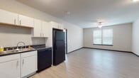 Located at 160–198 E Cottage Grove Rd in Cottage Grove, Wisconsin, this single-floor unit offers a well-organized, functional layout suited for everyday living. The open-concept kitchen and living area form the heart of the space, finished with light wood-style flooring throughout. The kitchen is equipped with white cabinetry, dark countertops, and black appliances, including a full-size refrigerator, dishwasher, electric range, and microwave. Ample upper and lower cabinet storage provides practical organization. A ceiling fan in the adjoining living area promotes air circulation, and a window with blinds allows natural light to fill the space.

The bedroom is carpeted for comfort and features a ceiling fan, a window overlooking the surrounding neighborhood, and generous wall space. The full bathroom includes a single-sink vanity with white cabinetry, a large mirror with overhead lighting, and a shower with tiled surround, all finished with light wood-style flooring that carries a clean, cohesive aesthetic.

A dedicated utility room houses a stacked washer and dryer along with storage shelving, offering added convenience within the unit. Overall, the space presents a clean, modern design with neutral tones throughout.