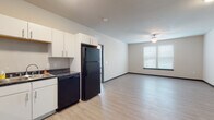 Located at 160–198 E Cottage Grove Rd in Cottage Grove, Wisconsin, this single-floor unit offers a well-organized, functional layout suited for everyday living. The open-concept kitchen and living area form the heart of the space, finished with light wood-style flooring throughout. The kitchen is equipped with white cabinetry, dark countertops, and black appliances, including a full-size refrigerator, dishwasher, electric range, and microwave. Ample upper and lower cabinet storage provides practical organization. A ceiling fan in the adjoining living area promotes air circulation, and a window with blinds allows natural light to fill the space.

The bedroom is carpeted for comfort and features a ceiling fan, a window overlooking the surrounding neighborhood, and generous wall space. The full bathroom includes a single-sink vanity with white cabinetry, a large mirror with overhead lighting, and a shower with tiled surround, all finished with light wood-style flooring that carries a clean, cohesive aesthetic.

A dedicated utility room houses a stacked washer and dryer along with storage shelving, offering added convenience within the unit. Overall, the space presents a clean, modern design with neutral tones throughout.