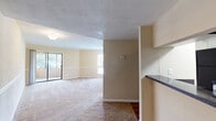This single-floor residence offers a functional and comfortable layout designed for everyday living. The open living area is finished with plush carpeting and features a decorative chair-rail molding detail along the walls, adding a classic touch to the warm, neutral color palette. Natural light fills the space through multiple windows, and a sliding glass door leads to an outdoor area, seamlessly connecting the interior to the outside. A textured ceiling adds subtle visual interest throughout the main living space.

The galley-style kitchen is well-appointed with white cabinetry, dark granite-style countertops, wood-look flooring, and black appliances including a full-size refrigerator. A pass-through counter connects the kitchen to the adjacent living area, enhancing the sense of openness and flow.

The bedrooms are carpeted and bright, each featuring ceiling fans with lighting, natural window views, and louvered bi-fold closet doors providing ample storage. The chair-rail molding detail is carried through these rooms, maintaining a cohesive aesthetic.

The bathroom is clean and straightforward, featuring a shower-tub combination with white tile surround, a toilet, and warm wood-look flooring. Overall, the space presents a well-organized, practical layout with consistent finishes throughout.