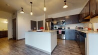 Located at 6921 University Ave in Middleton, Wisconsin, this single-floor residence offers a thoughtfully designed layout with modern finishes and a clean, contemporary aesthetic throughout.

The heart of the unit is an open-concept kitchen that serves as both a functional and visual centerpiece. It features a large central island with a light quartz countertop, ideal for dining or food preparation. Dark espresso and slate-blue cabinetry provide a striking two-tone contrast, complemented by a full suite of stainless steel appliances including a refrigerator, range, and over-the-range microwave. Stylish Edison-bulb pendant lights hang above the island, adding warmth and character to the space. Wood-look plank flooring runs throughout the kitchen and living areas, contributing to a cohesive and modern feel.

The bedrooms offer a comfortable retreat, finished with plush carpeting and windows with blinds that allow for natural light control. Each bedroom includes closet space, providing practical storage solutions.

The bathroom is well-appointed with a wide dual-sink vanity featuring dark cabinetry and brushed nickel hardware, a large wall mirror, and wood-look flooring that ties in with the rest of the unit. The layout is efficient and clean, with ample counter and storage space.

Overall, this residence presents a polished, move-in-ready living environment with consistent design choices and quality finishes throughout.