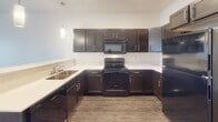 Located at 6019 W Yukon Trail in Sioux Falls, South Dakota, this single-floor unit offers a well-organized layout with a clean, contemporary aesthetic throughout. The open-concept kitchen serves as a central focal point, featuring rich dark espresso cabinetry paired with light countertops, a U-shaped configuration, and a full suite of black appliances including a range, microwave, dishwasher, and refrigerator. A peninsula with a breakfast bar extends into the adjoining living and dining area, where pendant lighting highlights the transition between spaces. Wood-look hard-surface flooring runs through the main living areas, adding warmth and durability.

The living area benefits from a sliding glass door fitted with vertical blinds, allowing natural light to fill the space while providing access to an outdoor area. Bedrooms are finished with plush carpeting and feature natural light from windows with blinds. At least one bedroom includes a walk-in closet with built-in shelving. The bathroom is equipped with a single-sink vanity featuring dark cabinetry and a marble-style countertop, a full tub-shower combination, wood-look flooring, and brushed nickel hardware and grab bars throughout, contributing to a cohesive and functional finish.