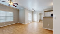 This single-floor residence features a cohesive, open layout unified by warm light wood flooring that extends throughout every room. The living area is generously proportioned, finished with crown molding, a ceiling fan, and track lighting. Multiple windows fitted with blinds allow ample natural light, and a glass-paned exterior door provides additional brightness and outdoor access. The space flows naturally toward a kitchen peninsula with a light stone-look countertop, offering a practical divide between the living and cooking areas.

The kitchen is well-appointed with white cabinetry, matching light countertops, and a full suite of black appliances including a range, over-range microwave, dishwasher, and refrigerator. A double sink is positioned under additional cabinetry, maximizing storage and functionality.

The bedrooms are comfortably sized, each with ceiling fans and windows that bring in natural light. At least one bedroom features a walk-in closet with built-in shelving. Two full bathrooms serve the residence, each featuring a tub-shower combination, white vanity cabinetry, light countertops, and wood-look flooring, with the primary bath including a large mirror and vanity lighting above the sink.