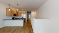This single-floor unit in Kenosha, Wisconsin offers a clean, modern aesthetic throughout, combining functional design with contemporary finishes. The open-concept layout connects the kitchen and living area seamlessly, creating a bright and cohesive space bathed in recessed lighting.

The kitchen is a standout feature, equipped with warm-toned wood cabinetry that extends to the ceiling for ample storage. A white subway tile backsplash adds a classic touch, while dark granite-style countertops provide a striking contrast. Stainless steel appliances — including a French door refrigerator with ice maker, a smooth-top electric range, and an over-the-range microwave — complete the kitchen suite. Pendant lights above the peninsula add both task lighting and visual interest, and an undermount stainless steel sink anchors the prep space.

The living area is generously proportioned, featuring warm wood-look flooring that carries throughout the unit, clean white walls, and ample natural light from a window. The open floor plan allows flexible furniture arrangements.

The bathroom is fitted with a walk-in shower enclosed by sliding glass doors with chrome hardware, reflecting a sleek, modern sensibility. Clean white walls and coordinating finishes maintain the cohesive design language found throughout the rest of the unit.