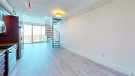 Located on the 24th floor at 215 North Pine Street in uptown Charlotte, this two-story loft unit offers a striking blend of modern design and urban living. The main level features an open-concept kitchen and living area with light hardwood-style flooring throughout. The kitchen is well-appointed with rich cherry wood cabinetry, granite countertops, a decorative tile backsplash, and a full suite of stainless steel appliances including a Bosch range, built-in microwave, and a large refrigerator. Track lighting runs along the ceiling, adding a contemporary touch. Floor-to-ceiling windows flood the living area with natural light and frame sweeping panoramic views of the Charlotte skyline and surrounding greenery. A sleek spiral staircase serves as both a functional and architectural centerpiece, connecting the main level to the upper floor. Upstairs, the generously sized primary bedroom is carpeted for comfort and features soaring ceilings, large windows, and access to the bathroom. A dedicated closet provides ample storage. A ceiling fan enhances comfort on the upper level, which also overlooks the city through expansive glazing. The unit includes a private balcony accessible from the main floor, offering unobstructed elevated views of the city.