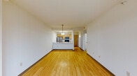 This single-floor residence offers a thoughtfully designed open-concept layout that maximizes both space and functionality. The living and dining area is finished with warm hardwood flooring throughout, complemented by clean white walls and a modern pendant light fixture. Large windows flood the space with natural light while framing sweeping urban views of the surrounding cityscape, creating a bright and airy atmosphere.

The kitchen is positioned in a semi-open configuration, accessible via a breakfast bar peninsula topped with a light stone-finish countertop and fitted with a stainless steel sink. Light wood cabinetry lines the kitchen walls and pairs with stainless steel appliances, including a refrigerator, over-the-range microwave, and a black electric range, providing a functional and cohesive aesthetic.

The bedroom is generously sized with plush wall-to-wall carpeting and benefits from a large corner window offering additional city views and ample natural light.

The bathroom features classic tile flooring, a full soaking tub with shower, a single vanity with matching light wood cabinetry and stone countertop, and a well-organized layout that leads to a dedicated storage or utility area. Throughout the space, the design is clean, practical, and well-maintained, making it a comfortable urban living environment.