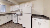 This single-floor residence offers a thoughtfully designed layout that balances comfort and functionality. The spacious living area is highlighted by wood-look flooring, a ceiling fan with light fixture, and multiple windows fitted with vertical blinds that allow ample natural light to fill the room. The open-concept kitchen is well-equipped with white shaker-style cabinetry, dark granite-look countertops, a full-size refrigerator, an electric range with overhead ventilation, and a dishwasher — all set atop durable wood-look tile flooring. A casual dining area adjacent to the kitchen provides additional versatility. The bedrooms feature plush carpeting, neutral-toned walls with accent colors, and large windows that bring in natural light and outdoor views. The primary bedroom includes the added convenience of dual closets. Bathrooms are finished with large-format gray tile surrounds in both the tub/shower and the separate walk-in shower, complemented by granite-look countertops and wood-look flooring. The textured ceilings throughout add a classic touch, while the clean, neutral palette creates a welcoming and move-in ready atmosphere throughout the home.