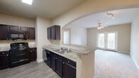 Located at 1300 Placid Cir in Waco, Texas, this single-story residence offers two bedrooms and two bathrooms within a well-organized floor plan. The open-concept kitchen connects seamlessly to the living area through a distinctive arched passageway, creating a sense of flow throughout the main living space. The kitchen is equipped with dark espresso cabinetry, granite-style countertops, a breakfast bar peninsula, a double sink, black appliances including a range and built-in microwave, and wood-look vinyl flooring. A closet off the kitchen provides convenient laundry or storage access. The living room features plush carpeting, a ceiling fan with light kit, track lighting, and French doors that invite natural light and outdoor views. Both bedrooms are carpeted and include ceiling fans, with the primary bedroom offering a generous footprint and natural light through blinds-covered windows. The two bathrooms are finished with tile-surround tub and shower combinations, including a sliding glass enclosure in the primary bath. Neutral warm-beige tones throughout the home create a calm, cohesive ambiance well-suited for comfortable everyday living.