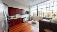 Located in Philadelphia's vibrant NoLibs neighborhood, this single-floor unit at 1401 N 5th St combines contemporary design with industrial character. Rich, deep-toned hardwood flooring runs throughout, creating a warm and cohesive aesthetic from the entry corridor to the main living area.

The open-plan living and kitchen space is the heart of the unit, anchored by a striking wall of large, grid-paned industrial windows that flood the room with natural light and offer open city views. The kitchen is well-appointed with deep mahogany cabinetry, granite countertops, and a full suite of stainless steel appliances, including a gas range, refrigerator, dishwasher, and microwave. A mounted flat-screen TV and bar-height seating add to the functional layout.

The living area provides a comfortable, well-lit space with room for seating and a central coffee table, making it ideal for relaxing or entertaining. Crown molding adds a refined architectural touch throughout.

The bathroom is thoughtfully finished with gray striped tile wainscoting, marble countertops, a dark wood vanity, and recessed medicine cabinet storage, creating a clean and polished aesthetic. A hallway with paneled white doors connects the living spaces, offering additional privacy and storage. The overall design balances urban edge with modern comfort.