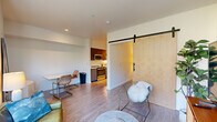 Located in Portland's vibrant Pearl District at 1470 NW Overton St, this one-bedroom, one-bathroom unit offers a thoughtfully designed layout that maximizes every square foot of living space. Light hardwood-style flooring flows throughout, tying each room together cohesively.

The galley kitchen runs along one side of the entry hallway and is outfitted with stainless steel appliances — including a refrigerator, electric range, and microwave — complemented by sleek cabinetry in both dark and blue-toned finishes, white tile backsplash, and ample counter space. Track lighting overhead keeps the workspace bright and functional.

The living room serves as the standout area of the home, anchored by dramatic floor-to-ceiling windows that flood the room with natural light and frame lush green treetop views. A wall-mounted HVAC unit ensures year-round comfort. A distinctive sliding barn door separates the bedroom from the main living area, adding a modern, space-saving design element.

The bedroom is a quiet, private retreat featuring a sliding closet with built-in shelving and warm-toned flooring. The bathroom is clean and efficient, offering a full tub-shower combo, a single vanity with undermount sink, and tile flooring throughout.