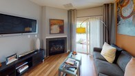 This well-appointed single-floor residence combines contemporary design with functional living spaces. The living room serves as a welcoming centerpiece, featuring a corner gas fireplace framed in dark tile, warm hardwood flooring, and sliding glass doors that open to a private patio with lush outdoor views. Bold orange accent walls appear throughout the home, adding warmth and visual contrast against the cool gray tones found in most rooms.

The kitchen is outfitted with dark espresso cabinetry, granite countertops, and a full suite of stainless steel appliances, including a range with overhead microwave and a full-size refrigerator. The adjacent dining area features a bold orange accent wall adorned with large framed mirrors, creating a sense of depth and brightness, complemented by a modern pendant light fixture overhead.

The bedrooms are carpeted for comfort, each benefiting from natural light through large windows with outdoor views. One bedroom showcases an eye-catching upholstered headboard and direct access to a private bathroom. A walk-in closet with built-in shelving adds practical storage. The bathroom includes a full soaking tub with white subway tile surround, accented by a decorative mosaic border tile for an elegant finishing touch.