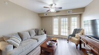 This single-floor, 3-bedroom, 2-bathroom unit offers a practical and well-organized layout across its efficiently designed footprint. The open-concept living and dining area forms the social core of the space, featuring wood-look plank flooring, neutral warm-beige walls, and a ceiling fan overhead. The living room is brightened by a set of French doors that invite natural light and provide outdoor access, creating an airy, connected atmosphere. The adjacent dining area is defined by a pendant light fixture hanging above a central dining table, with a closet conveniently located nearby.

The kitchen is outfitted with warm honey-toned cabinetry extending to the ceiling, granite-style countertops, stainless steel appliances including a refrigerator, range, microwave, and dishwasher, and a double sink. Track lighting illuminates the workspace effectively.

The spacious primary bedroom features plush carpet flooring, a ceiling fan, and a double panel closet door. The two bathrooms include vanities with warm wood cabinetry, white countertops, large mirrors, and over-toilet storage cabinets. The two additional bedrooms are modest in scale, each with neutral finishes and hard-surface flooring, suitable for varied uses.