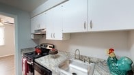 Floor Plan B is a single-floor residence designed with functionality and comfort in mind. The kitchen serves as a focal point of the home, showcasing granite-style countertops with warm, earthy tones that provide ample workspace for cooking and meal preparation. White upper cabinetry with brushed nickel hardware lines the walls, offering generous storage while maintaining a clean and bright aesthetic. A stainless steel sink with a modern pull-style faucet is seamlessly integrated into the countertop, complementing the kitchen's cohesive design. The electric range with a built-in overhead ventilation hood adds to the kitchen's practical layout, making it well-equipped for everyday use. The white cabinetry and light-toned surfaces work together to reflect light and create an open, airy feel within the space. The overall design of Floor Plan B emphasizes efficient use of space without sacrificing style, making it a well-appointed option for those seeking a straightforward, move-in-ready residence. The thoughtful layout and consistent finishes throughout contribute to a welcoming and organized living environment.
