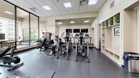 Located on Griswold Street in the heart of Detroit, MI, this fitness center offers a comprehensive exercise facility designed to support a full range of workout routines. The space is thoughtfully laid out across a single floor, providing ample room for both cardio and strength training activities.

The exercise room features a drop-panel ceiling with recessed lighting that keeps the space bright and well-illuminated throughout. Large arched windows along one wall invite natural light and provide views of the surrounding urban environment, contributing to an open and energizing atmosphere. Decorative columns add an architectural character that balances the functional nature of the space.

The cardio zone is well-appointed with multiple elliptical trainers, treadmills, and stationary bikes, all lined up to accommodate several users simultaneously. Mounted flat-screen TVs are positioned throughout, providing entertainment during workouts. For strength training, the facility includes a multi-station cable machine, a full rack of dumbbells displayed on tiered shelving, and adjustable benches, supported by full-length mirrors that enhance the sense of space. Built-in shelving units along the wall offer convenient storage for personal items and accessories.

The floors are covered in durable rubber flooring, practical for both heavy equipment and high-impact activity. A glass-paneled door provides an elegant entry point, while subtle decorative touches such as potted plants and framed artwork give the space a polished, welcoming feel.