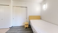 This compact unit at 304 College Ave in Ithaca, NY is thoughtfully designed to maximize functionality within a modest footprint. The single-floor layout incorporates a bedroom, kitchen, and full bathroom, each clearly defined despite the efficient use of space.

The bedroom features patterned carpet flooring, crisp white walls, and a wall-mounted light fixture. A large sliding-door closet provides ample storage, while a window allows natural light to enter, creating a bright and comfortable atmosphere. The room accommodates a bed, dresser, desk, and small dining area, demonstrating versatile use of the available space.

The kitchen area is positioned near the entry and features light wood cabinetry, a granite-style countertop, a stainless steel sink, and wood-look vinyl flooring. The solid entry door is equipped with a keypad lock, adding a layer of security and modern convenience.

The bathroom is clean and accessible, featuring wood-look tile flooring, white walls, a glass-partitioned shower with grab bars, and a toilet. The accessible design elements suggest thoughtful planning for a range of occupants.

Overall, the unit presents a clean, modern aesthetic with practical finishes suited for single occupancy living in the College Ave corridor of Ithaca.